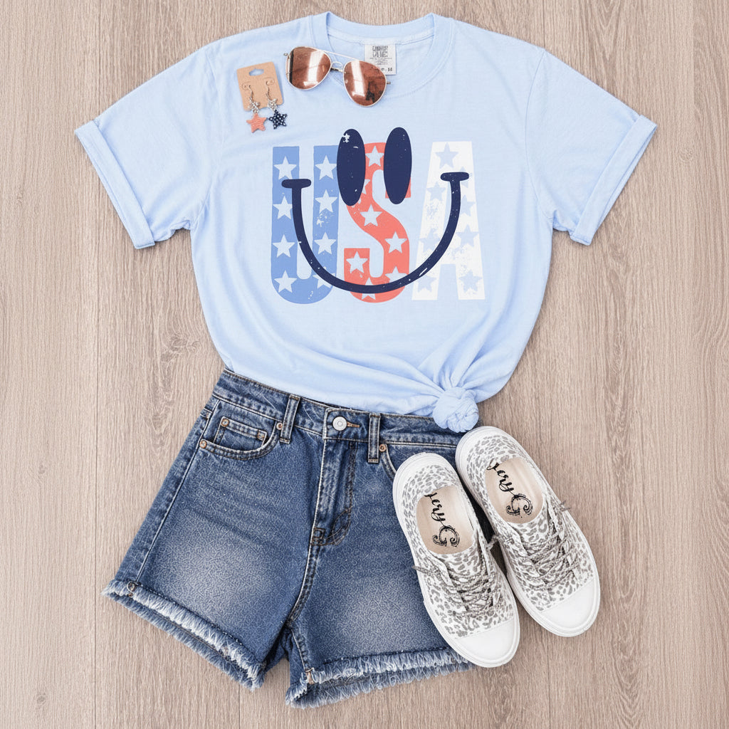 Light blue t-shirt with 'USA' design, denim shorts, and sparkly sneakers on a wooden surface