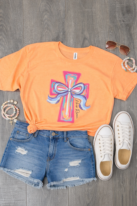 Peach He Is Risen painted cross graphic tee with colorful bow design styled with denim shorts and white sneakers flat lay
