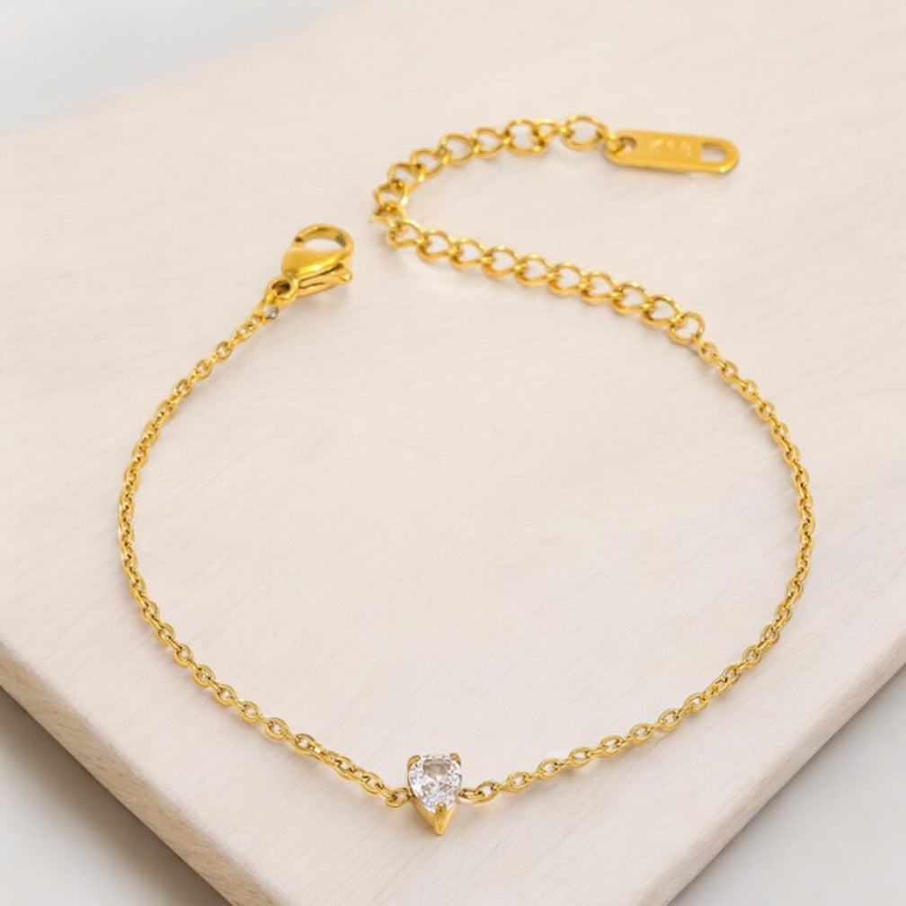 Gold bracelet with a pear-shaped diamond on a beige background