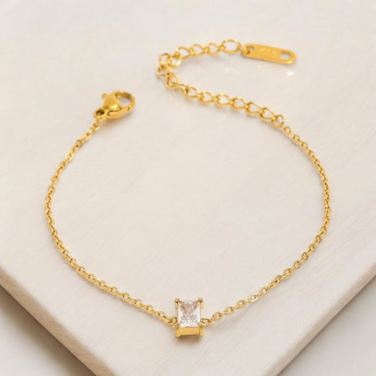 Gold bracelet with an emerald-cut gemstone on a light beige background