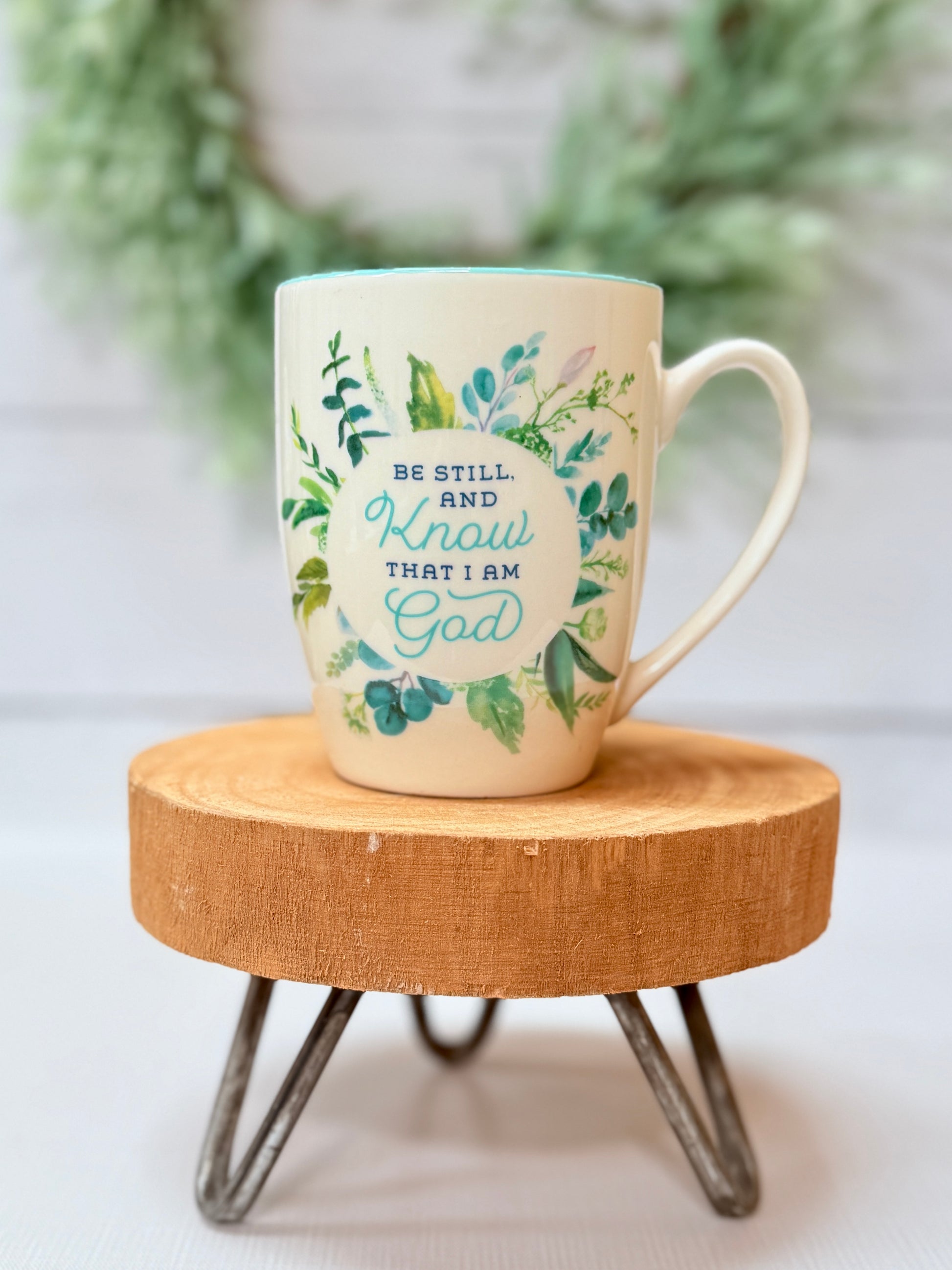 Be still and know turquoise floral coffee mug with soft turquoise tones styled on a wooden stool with greenery background