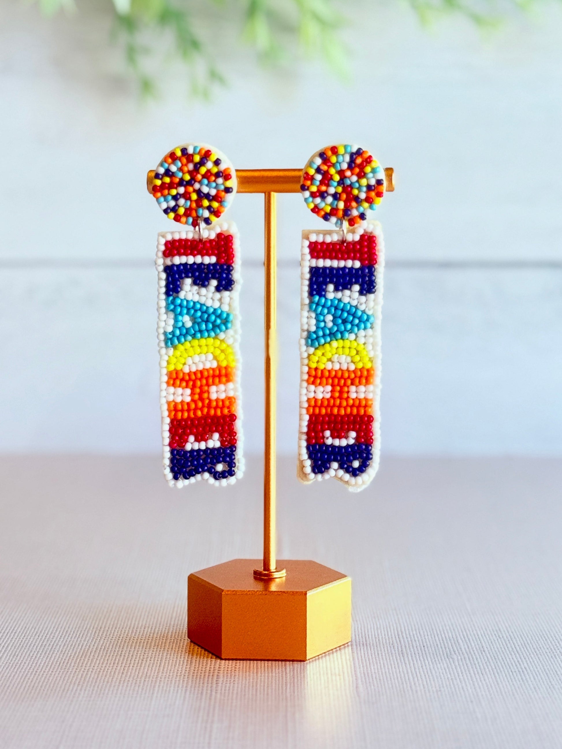 Colorful beaded “Teacher” earrings on a stand with a light background
