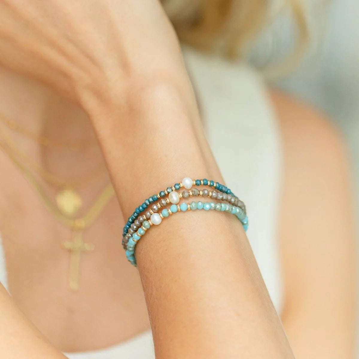 Close-up of a person's arm wearing multiple beaded bracelets on a neutral background